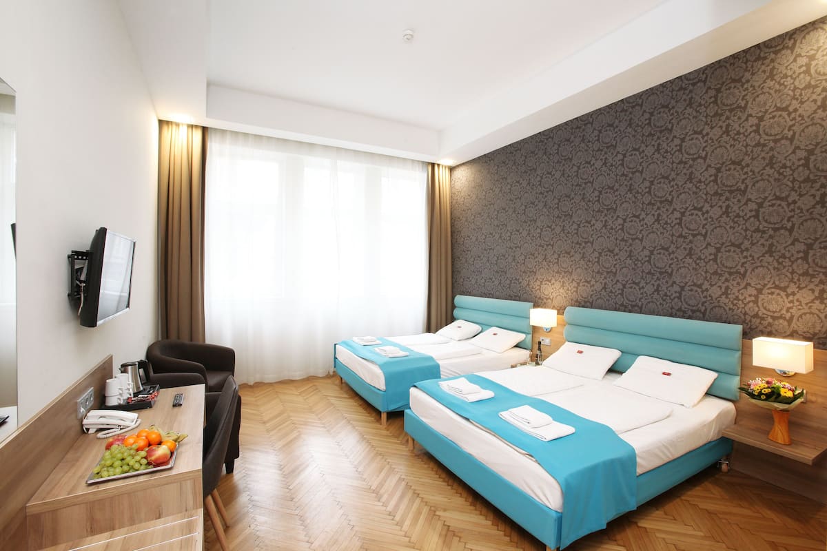 Une chambre d’hôtel avec deux lits, un bureau sur lequel se trouve une corbeille de fruits, une télévision et un mur décoré d’un motif.