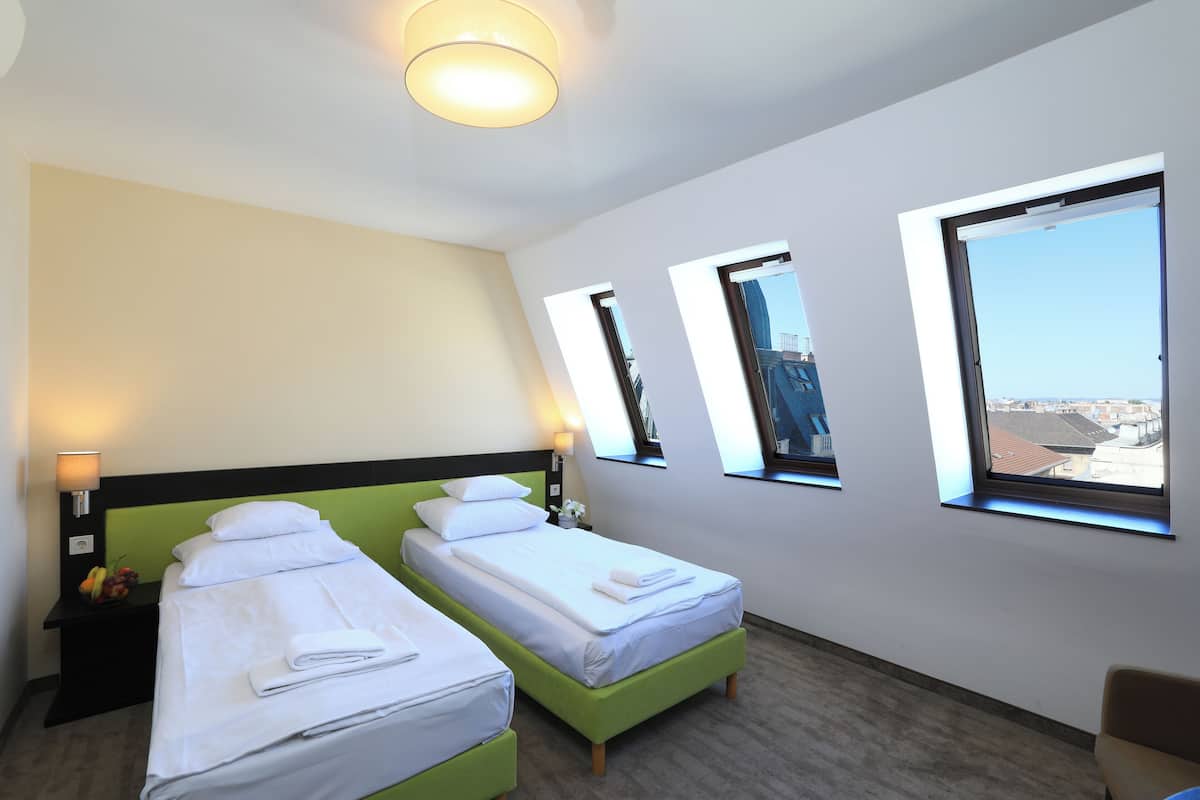 Une chambre d’hôtel avec deux lits simples, une table de chevet avec une lampe et une vue sur la ville par les fenêtres.