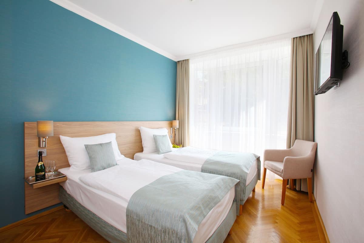 Une chambre d’hôtel avec deux lits, un téléviseur fixé au mur, une chaise et une fenêtre avec des rideaux.