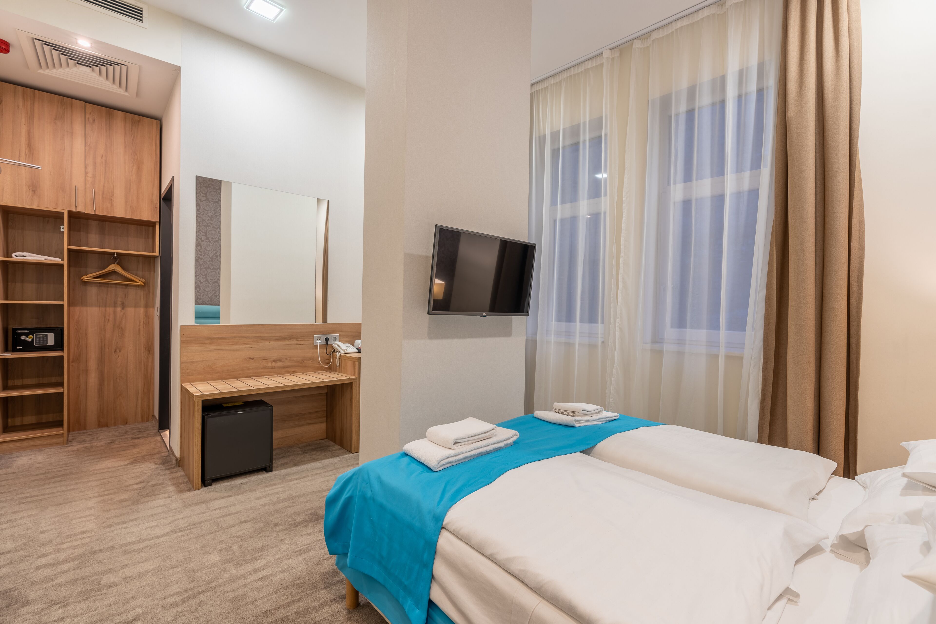A hotel room with a bed, a desk, a wardrobe, and a TV.