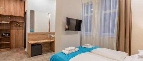 A hotel room with a bed, a desk, a wardrobe, and a TV.