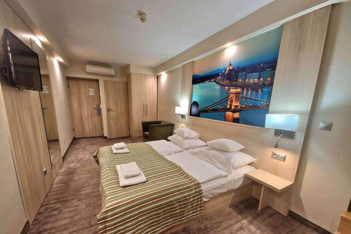 Une chambre d’hôtel avec un lit, un bureau, une chaise, une télévision et un tableau représentant un pont.