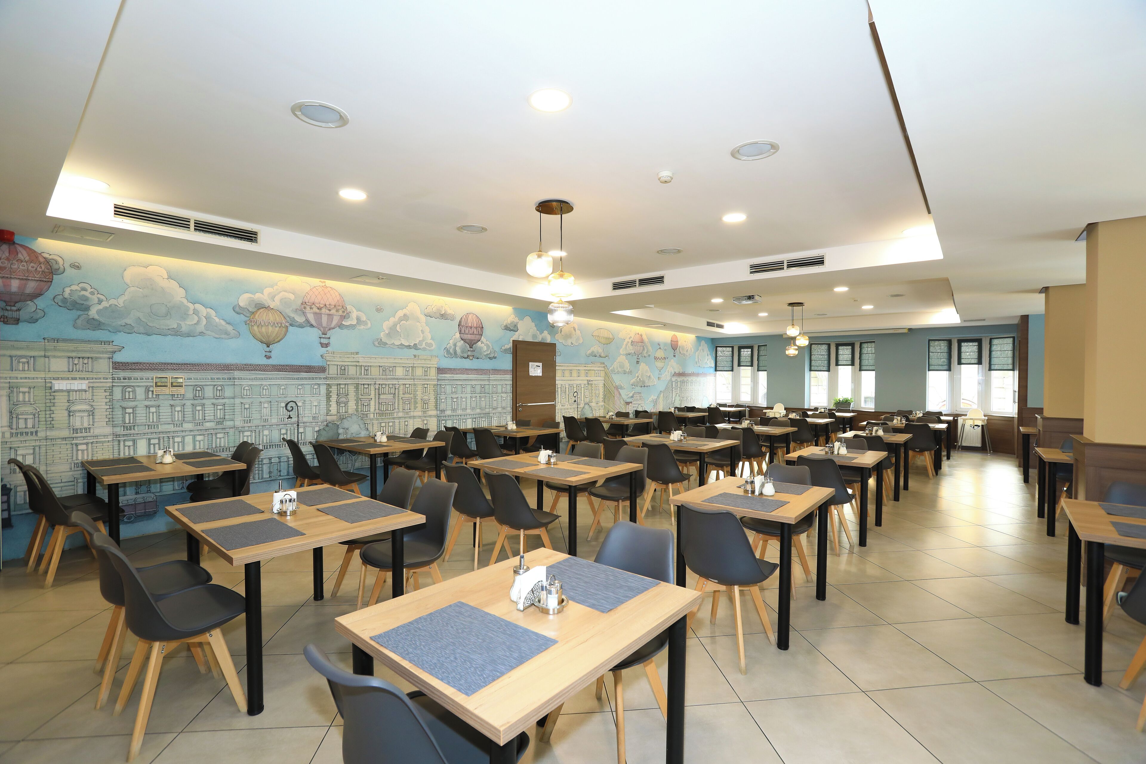 A dining area with tables and chairs, a mural on the wall, and ceiling lights.