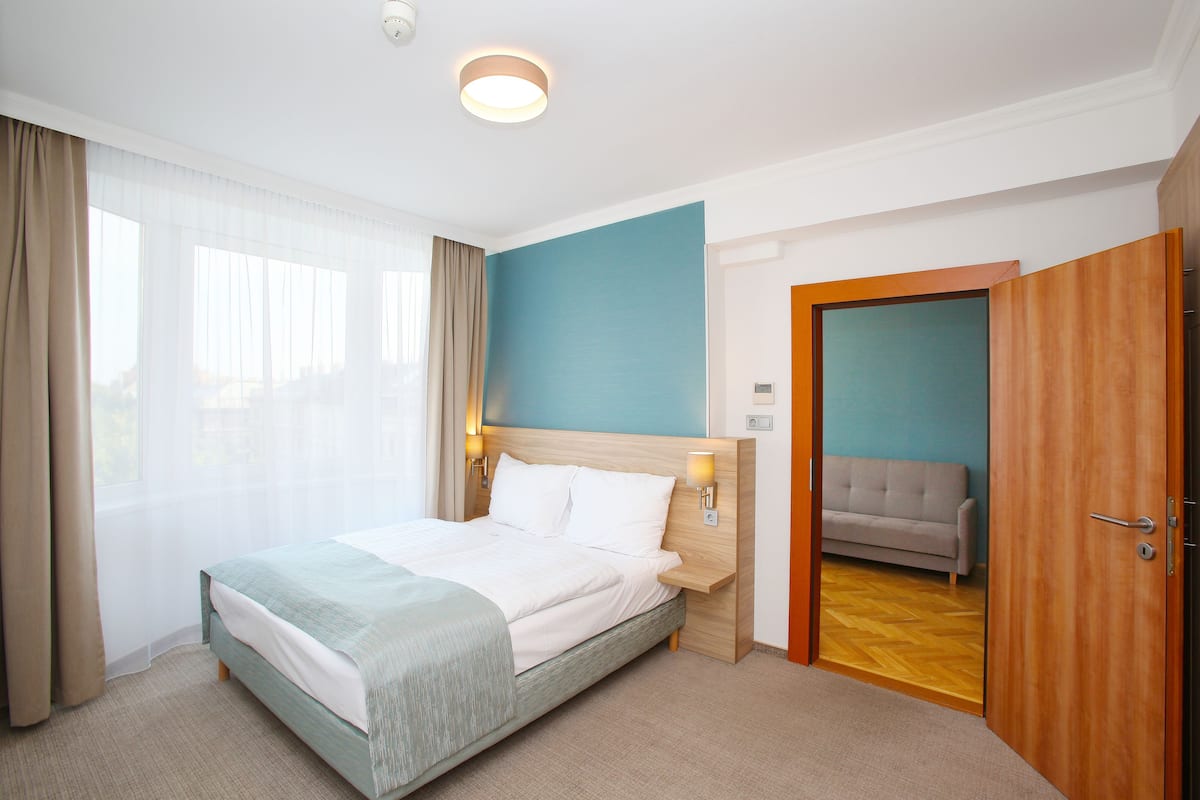 Une chambre d’hôtel avec un lit, un canapé, une porte en bois et une vue sur la ville par la fenêtre.