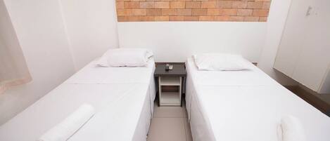 Habitación doble con dos camas, una mesita y una pared de ladrillo.