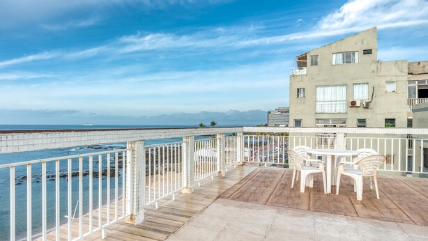 A balcony with a view of the sea and mountains, white chairs, and a table. - Rede Andrade Ondina Hotel (Salvador)