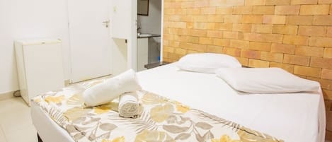 Habitación de hotel con cama, una puerta blanca, pared de ladrillo y baño a la vista a través de una puerta abierta.