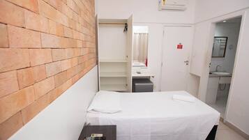 Habitación de hotel con pared de ladrillo, cama con ropa blanca, una mesita con un control remoto y baño con lavamanos y espejo.