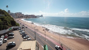 A coastal road with a beach on the right, lined with parked cars and a pedestrian path. - Rede Andrade Ondina Hotel (Salvador)