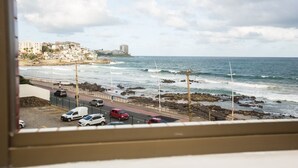 A coastal view with a road leading to the beach, parked cars, and buildings in the background. - Rede Andrade Ondina Hotel (Salvador)