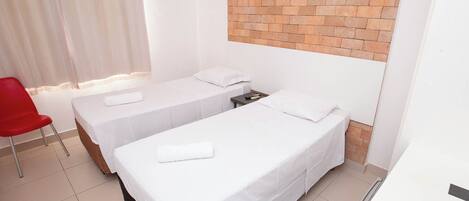Una habitación de hotel con dos camas individuales, una silla roja y una pared de ladrillo decorativa.