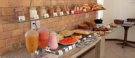 Un bufé con diversos alimentos y bebidas, incluyendo frascos con salsas y una selección de panes y pasteles.