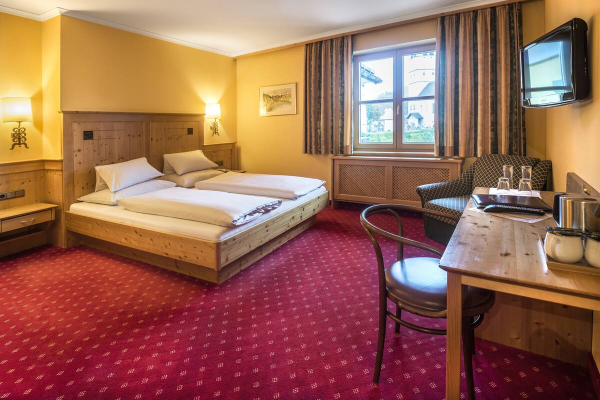 A hotel room with a double bed, a desk with a chair, a television, and a window with curtains.
