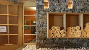 Pared de piedra con repisas que sostienen toallas enrolladas, piso de madera y puerta con un cartel que indica una zona tranquila.