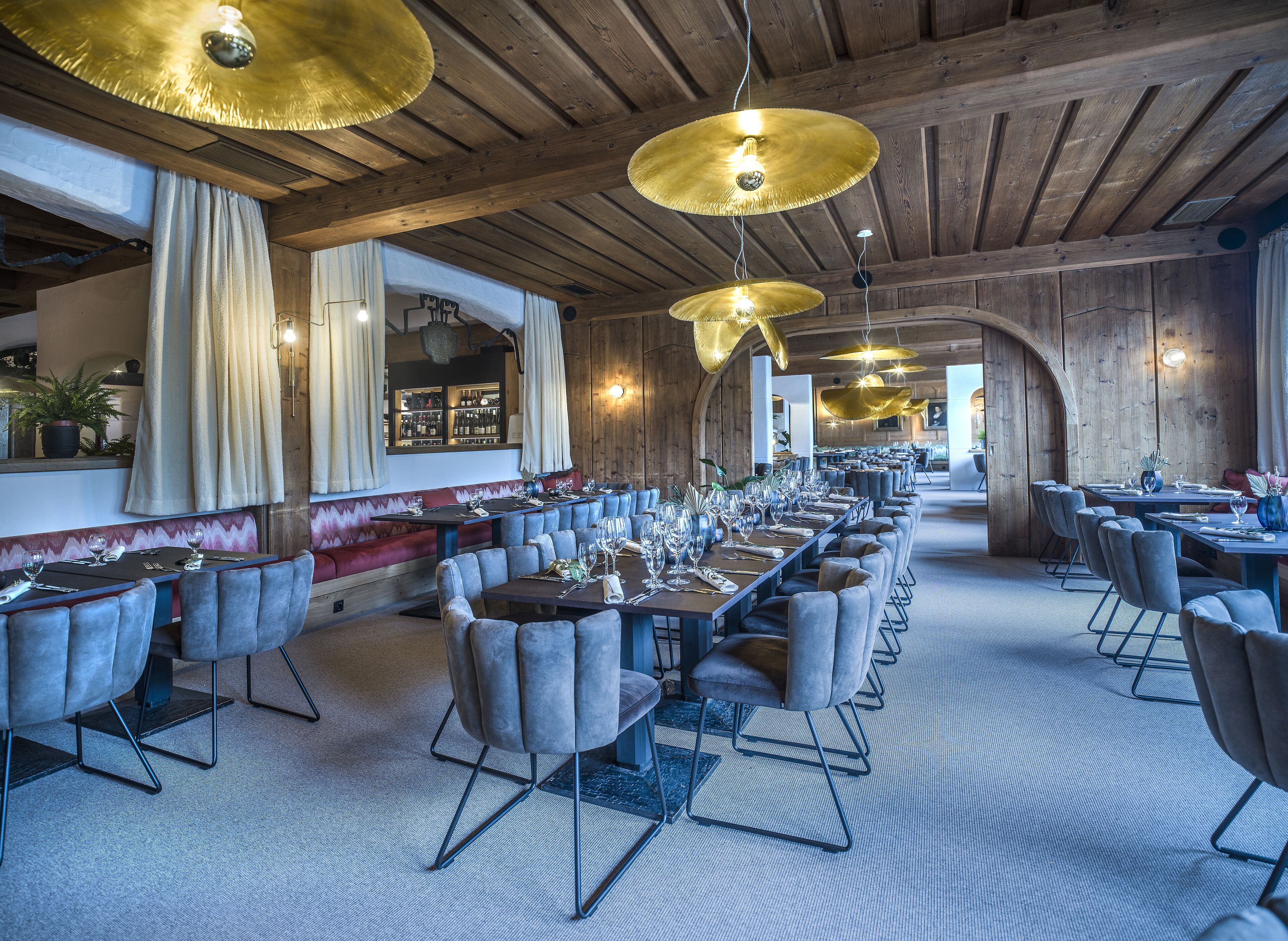Ein Restaurant mit langen Gemeinschaftstischen, gepolsterten Sitzgelegenheiten und herabhängenden Goldlampen.