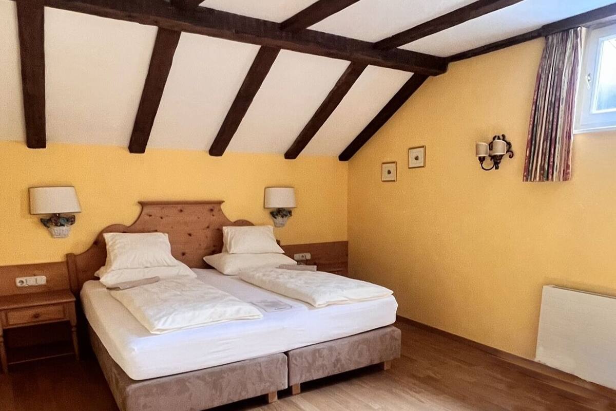 A double bed with two nightstands, a wooden ceiling, and a window with curtains.