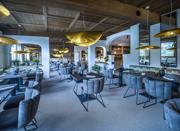 A spacious restaurant with high ceilings, modern furniture, and large pendant lights. - Hotel Tiefenbrunner (Kitzbuhel)