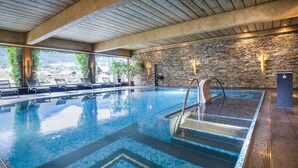 Piscina interior con agua cristalina, pared de piedra y vista a zonas verdes.