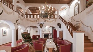Un vestíbulo amplio con candelabro, sillones de cuero rojo, chimenea y una escalera.