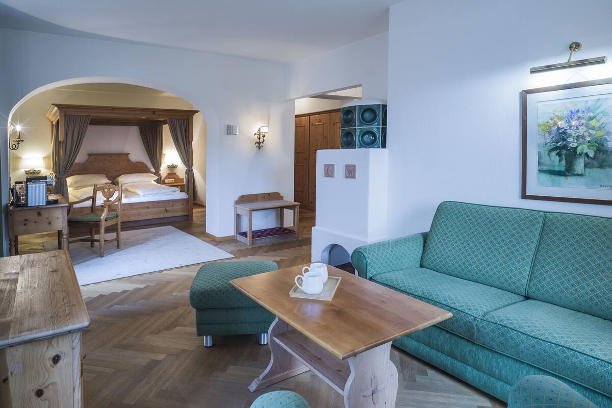 A cozy room with a bed, a green sofa, a wooden table, and a small table with a cup.