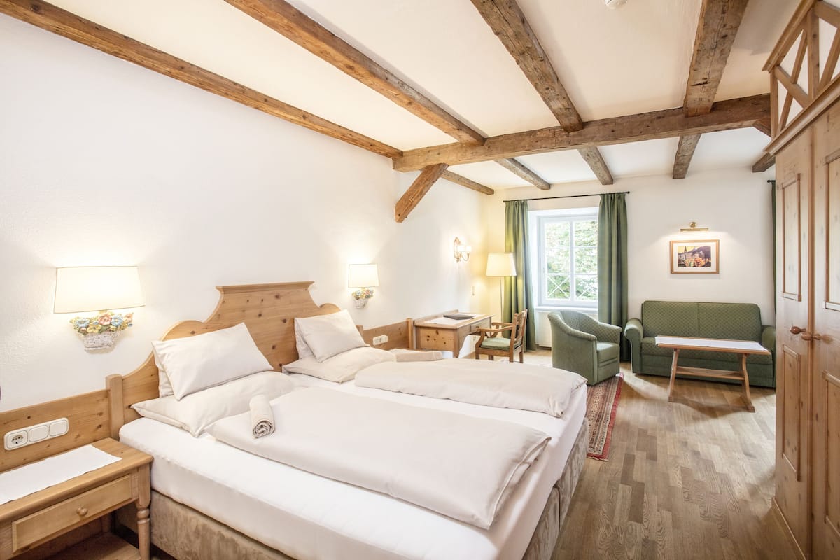 A room with two beds, wooden beams on the ceiling, a green sofa, and a small table.