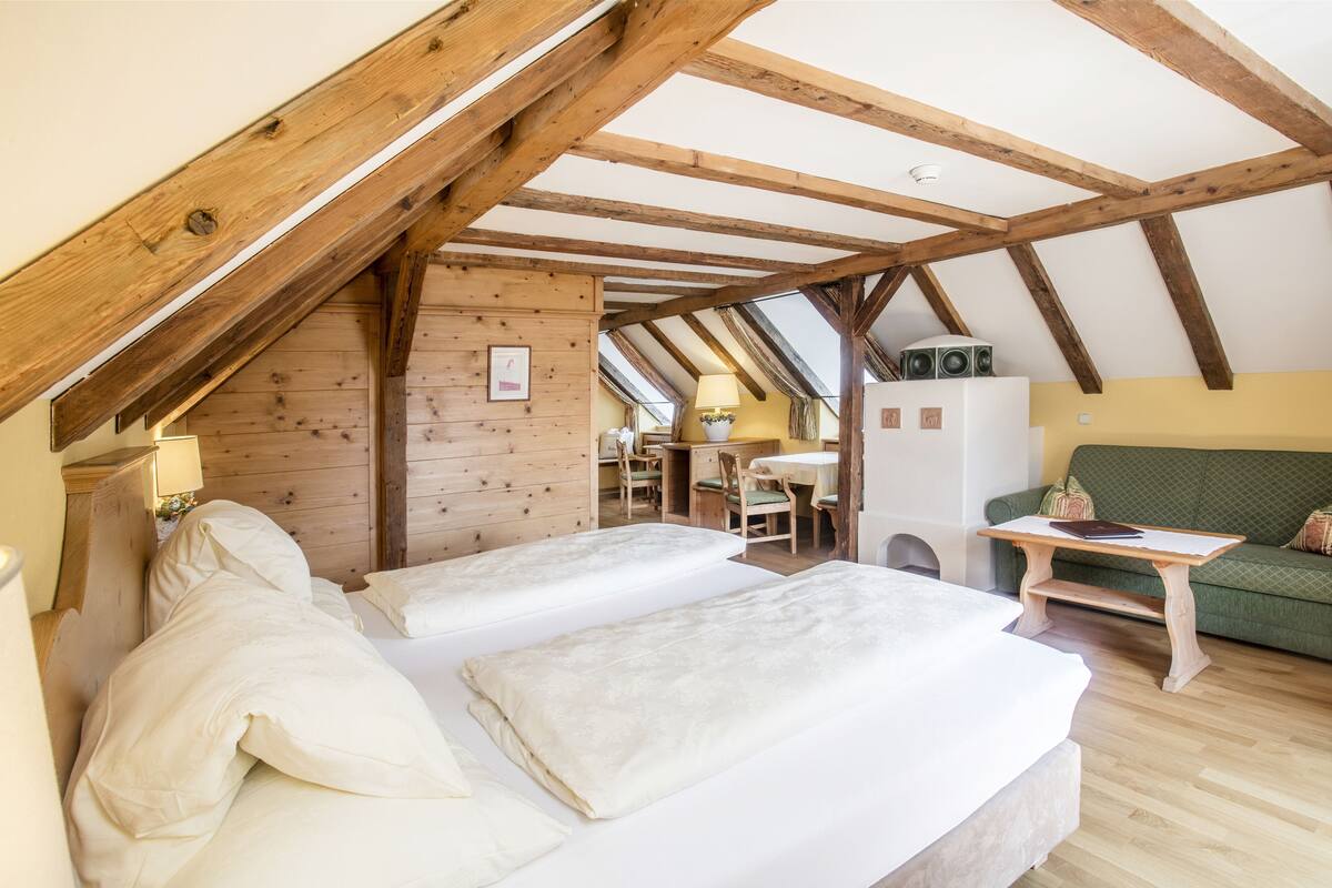 A cozy attic bedroom with two beds, wooden beams, a green sofa, and a small table.