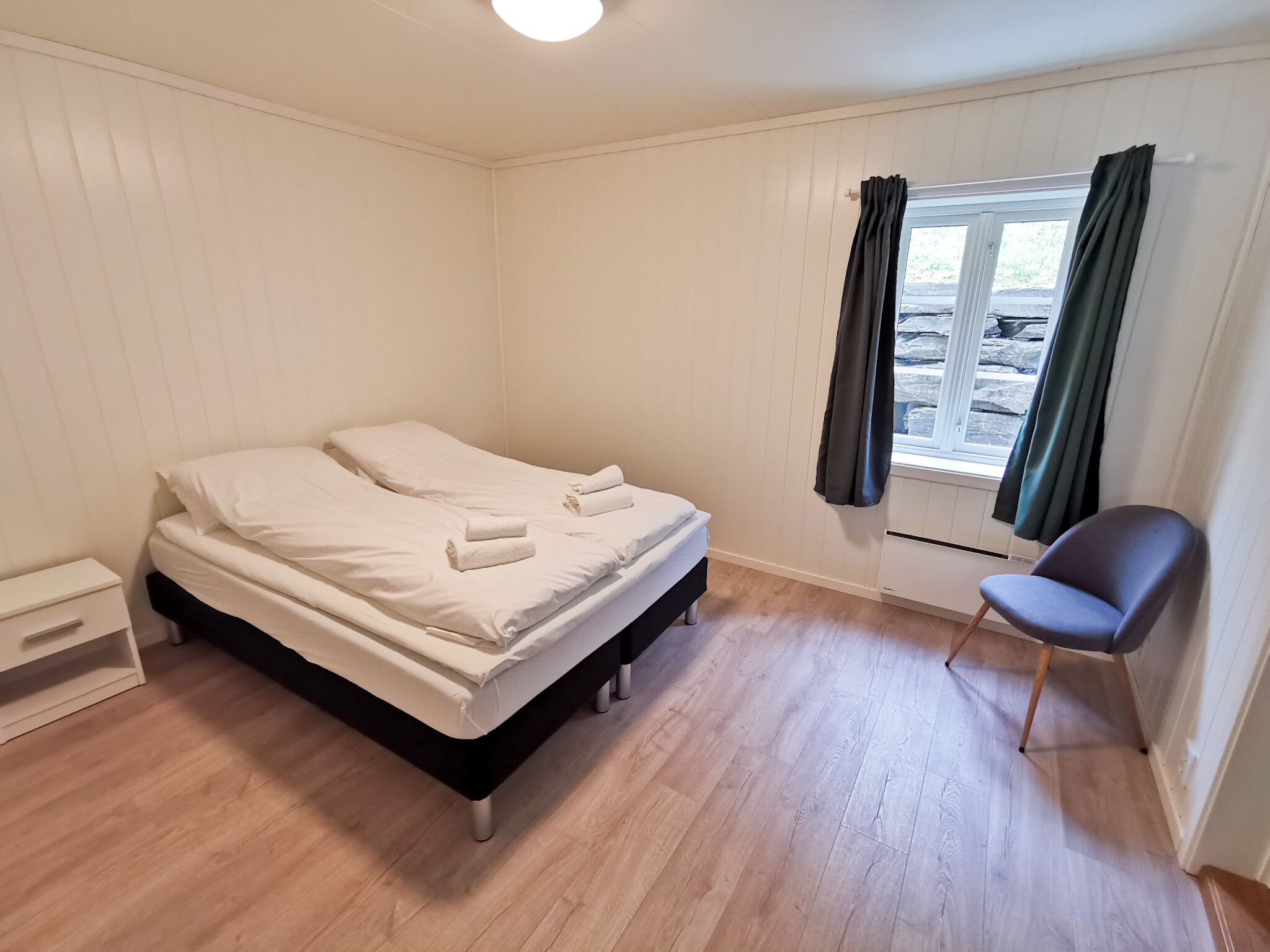 A bedroom with a bed, a chair, a nightstand, and a window with curtains.