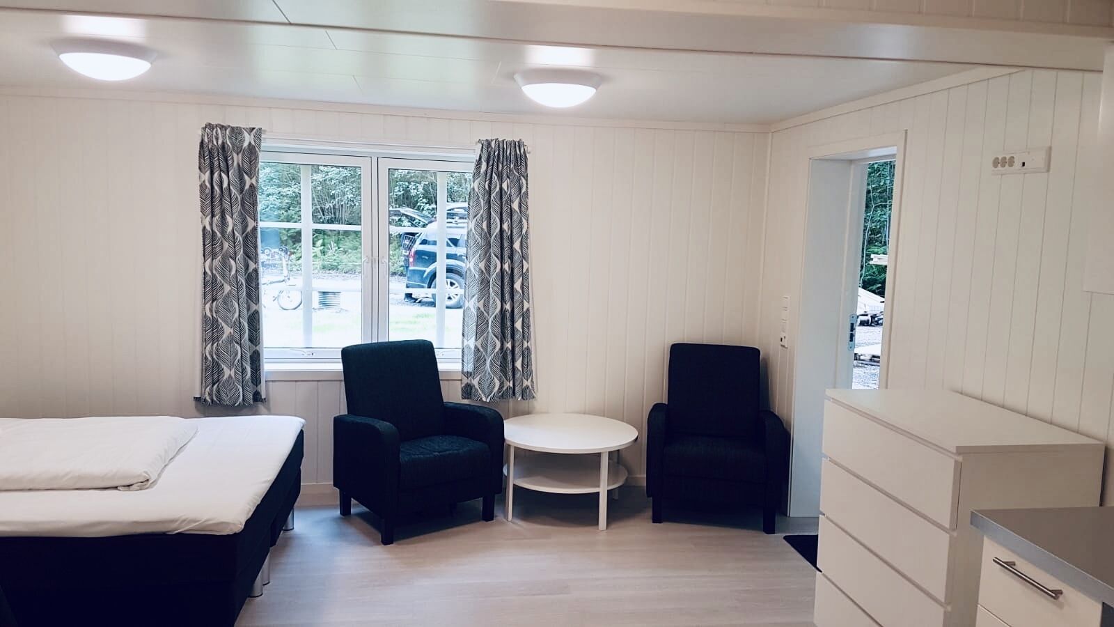 Una habitación con una cama, dos sillones, una mesita y una ventana con cortinas.