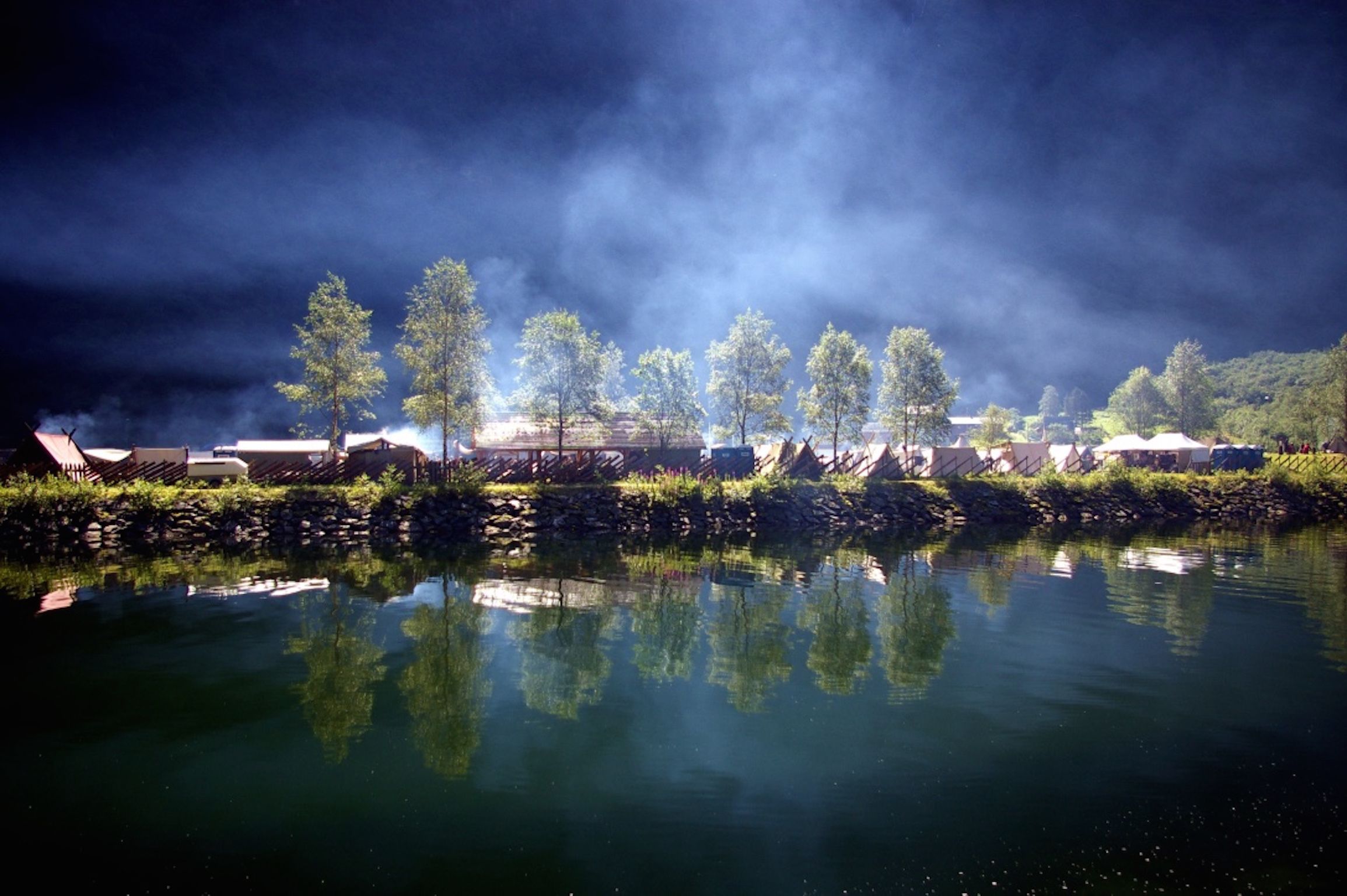 A riverside view with stone walls and trees reflecting on the water.