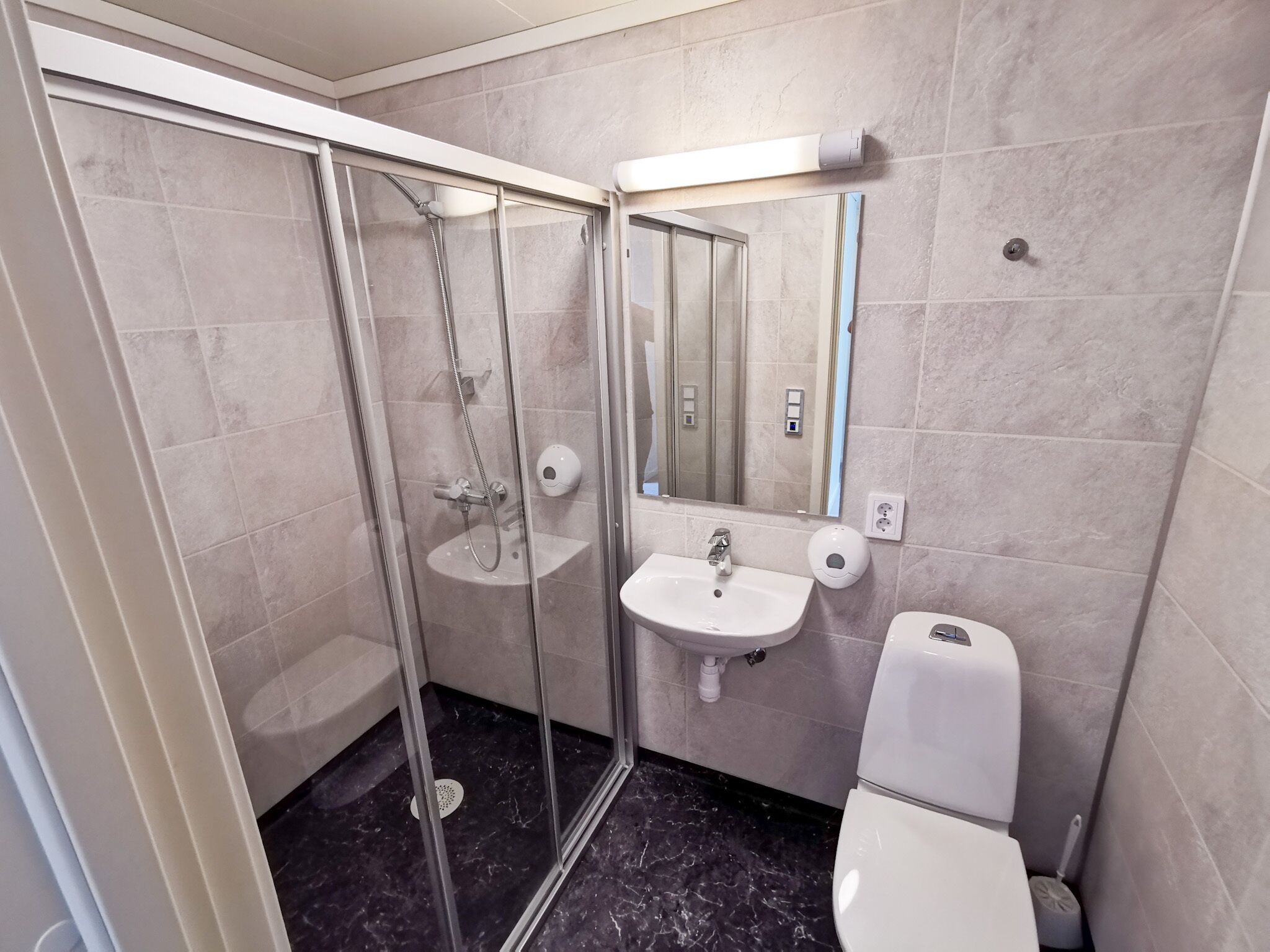 Un bany modern amb dutxa de vidre, un envàs de rentapès i un vàter.