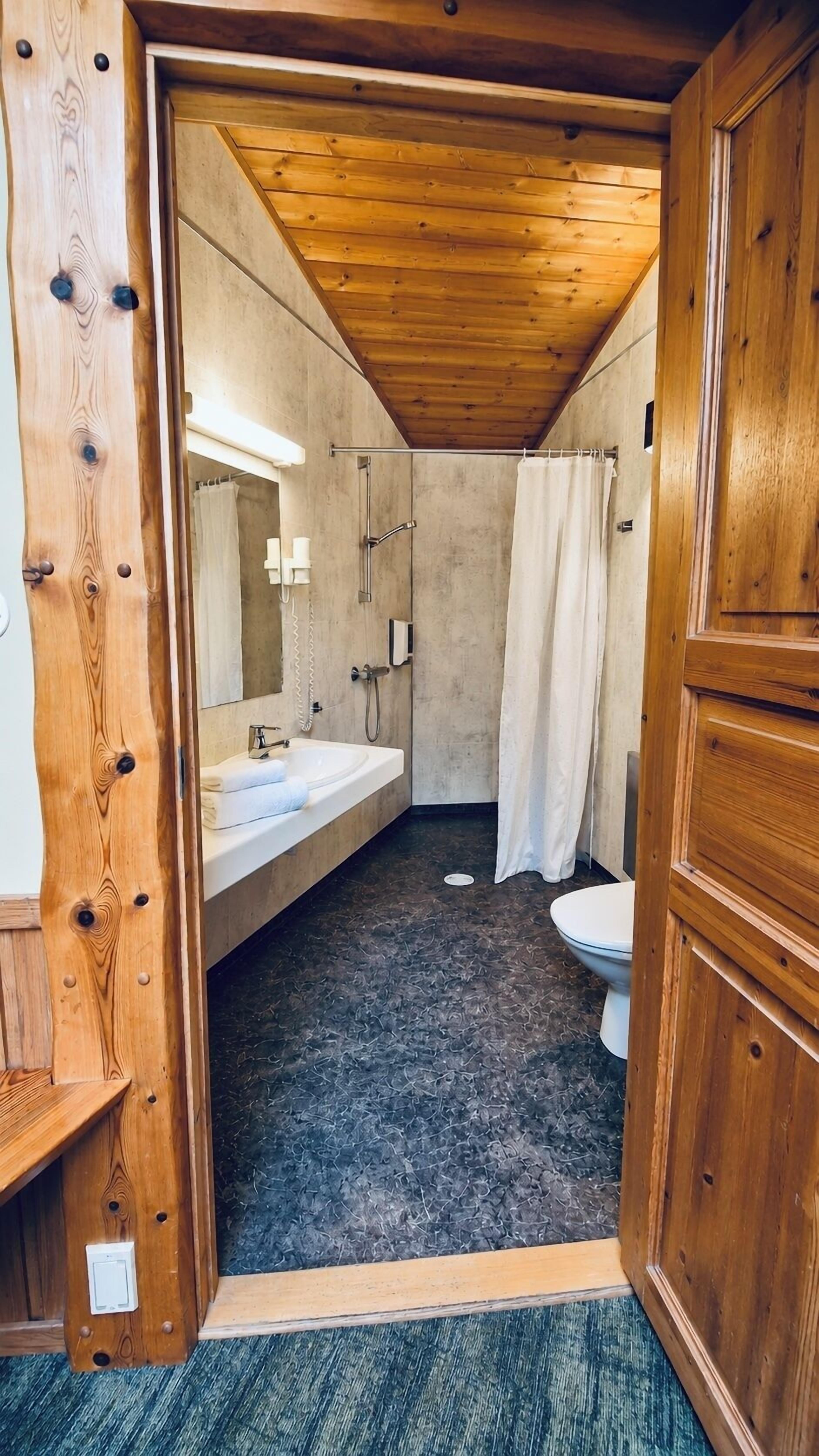 A wooden-paneled bathroom with a shower, a sink, and a toilet.