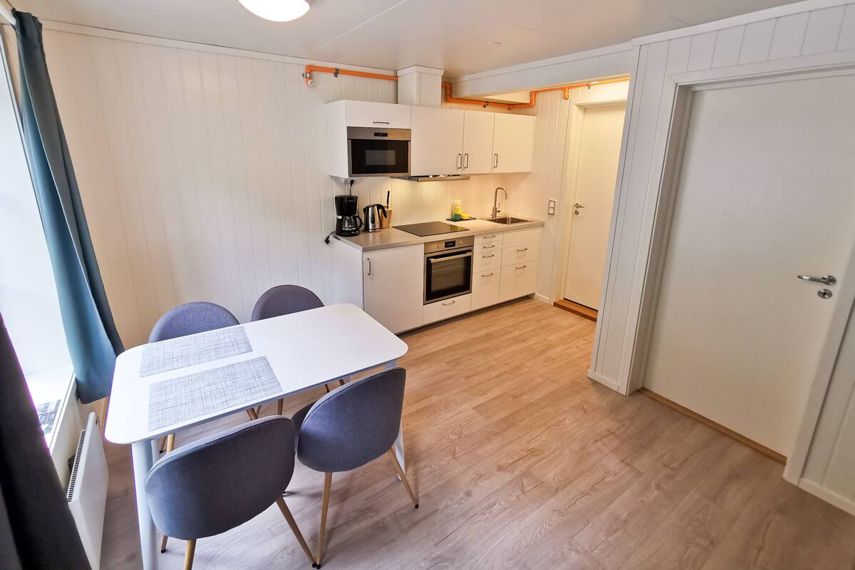 Cocina compacta con armarios blancos, microondas, cafetera y pileta.