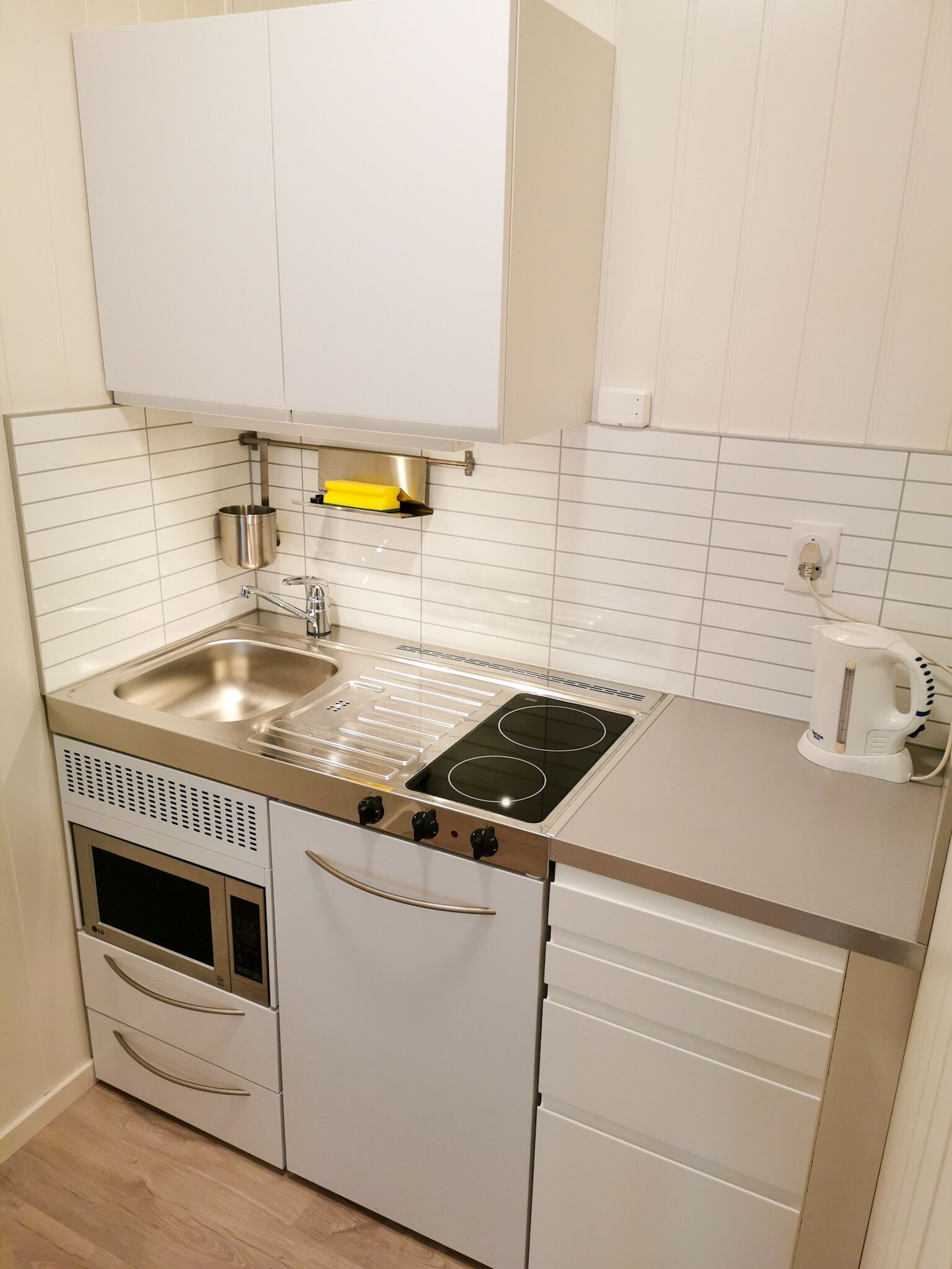 A compact kitchen with a stainless steel stove, a sink, and a kettle.
