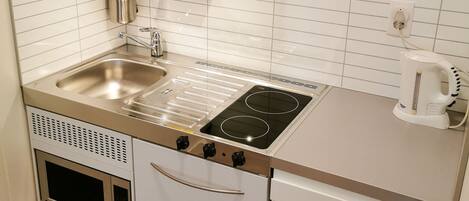 A compact kitchen with a stainless steel stove, a sink, and a kettle.