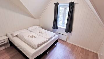 A bedroom with a bed, a nightstand, a window with curtains, and a radiator.
