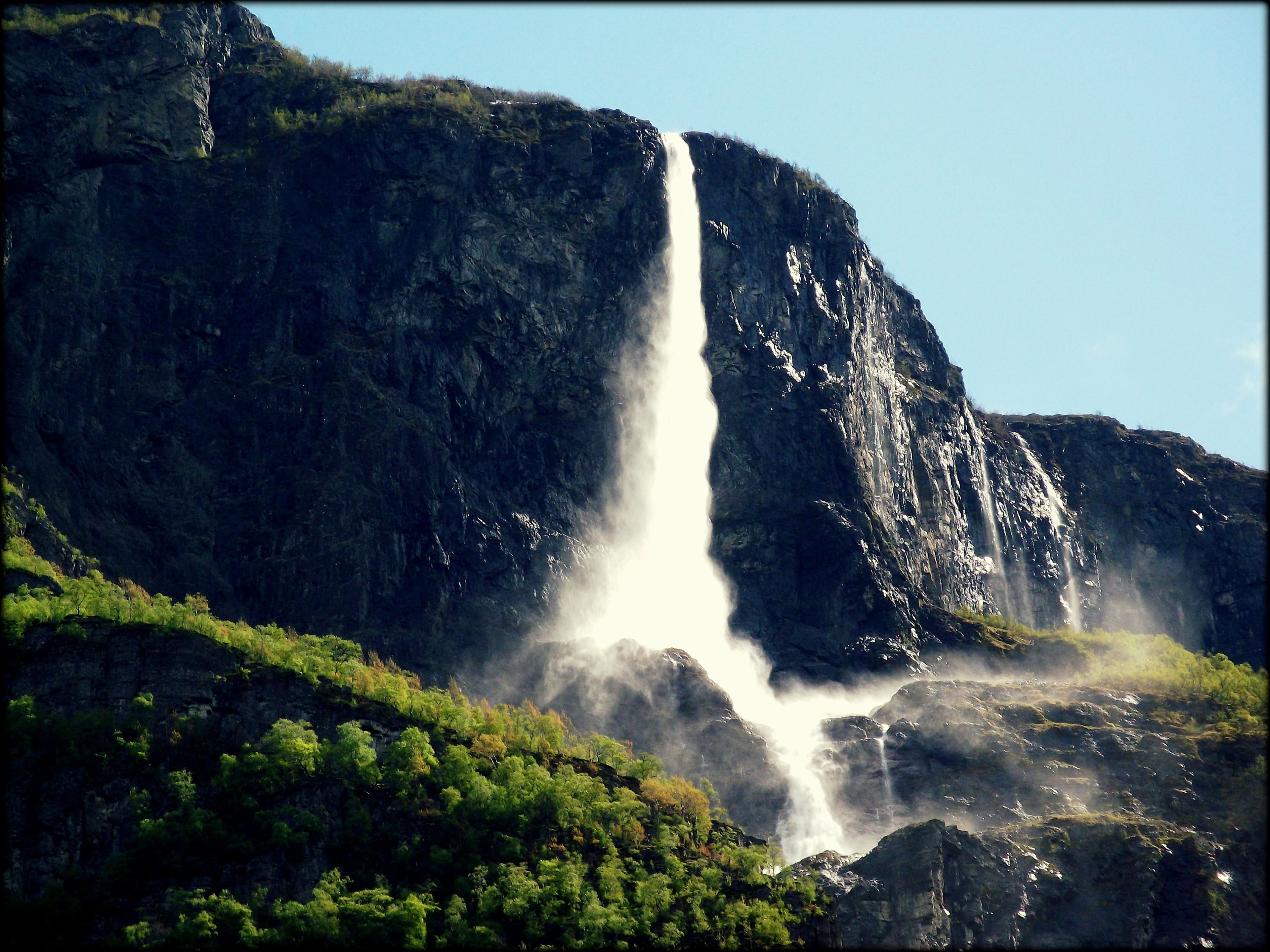 Una cascada que flueix sobre un penya-segat rocosós, envoltat de vegetació exuberant.