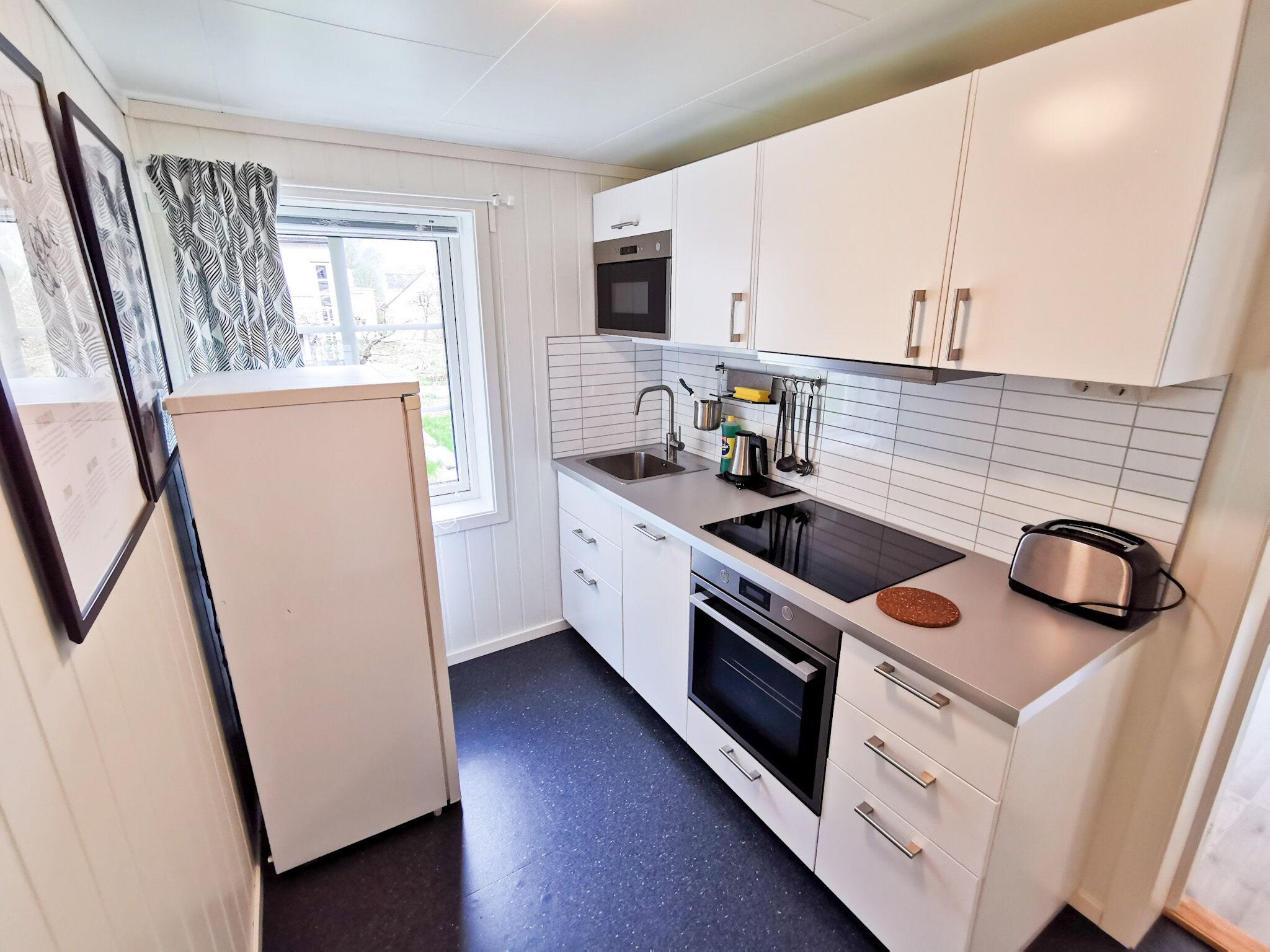 A compact kitchen with white cabinets, a black stove, a sink, and a toaster.
