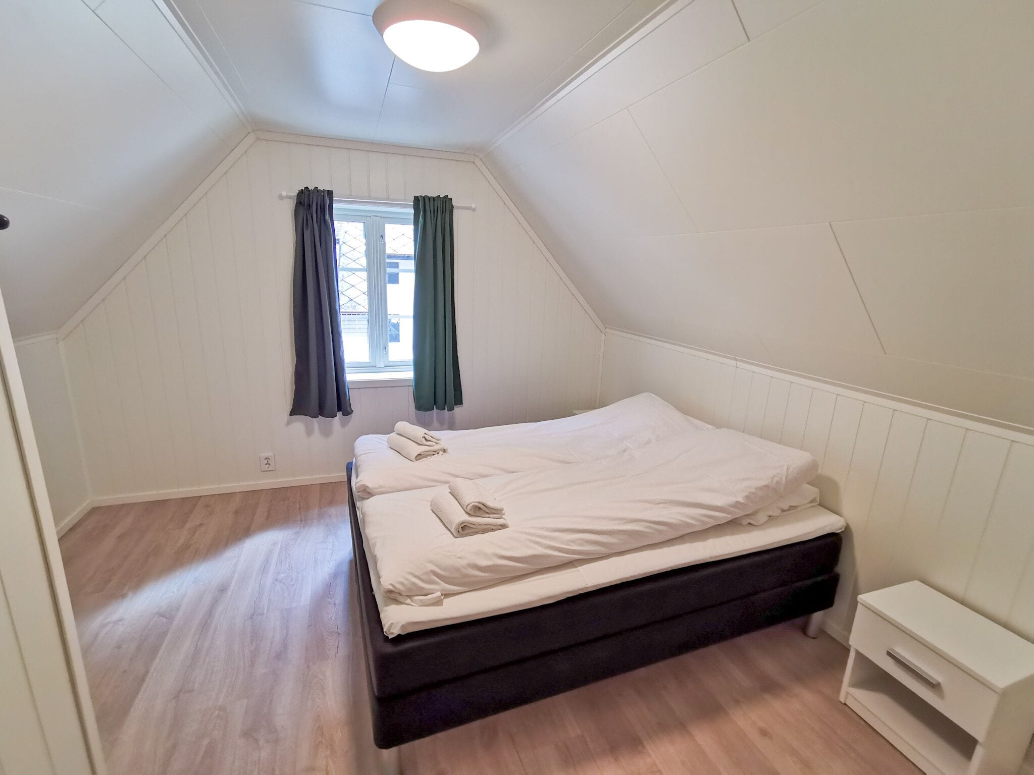 A small, clean room with a single bed, a nightstand, and a window with curtains.