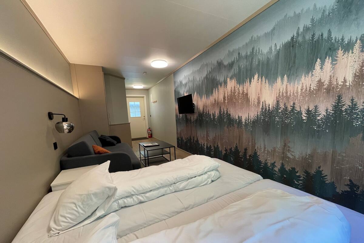 Una habitación de hotel con cama, sofá, una mesita y un mural en la pared con un bosque.
