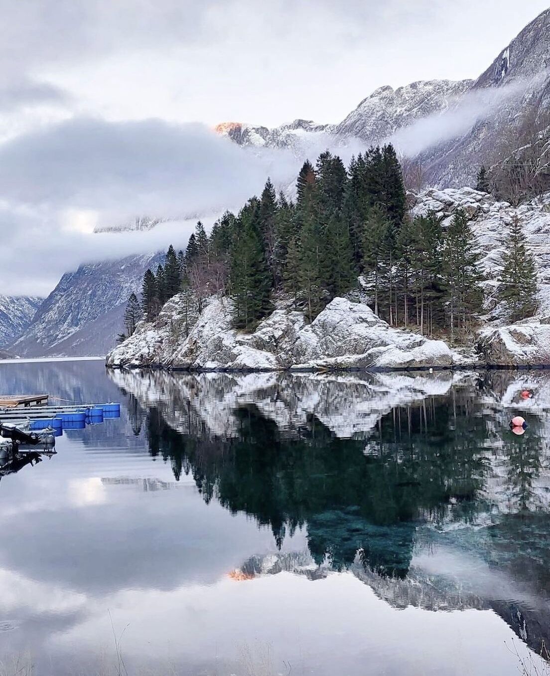 Un lago tranquilo con montañas nevadas y un bosque al fondo.