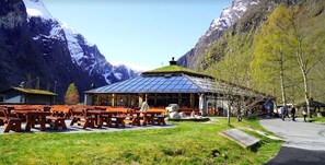 Un chalet de montagne doté d’une salle à manger avec un toit en verre, de bancs en bois et d’un sentier menant à une allée couverte.
