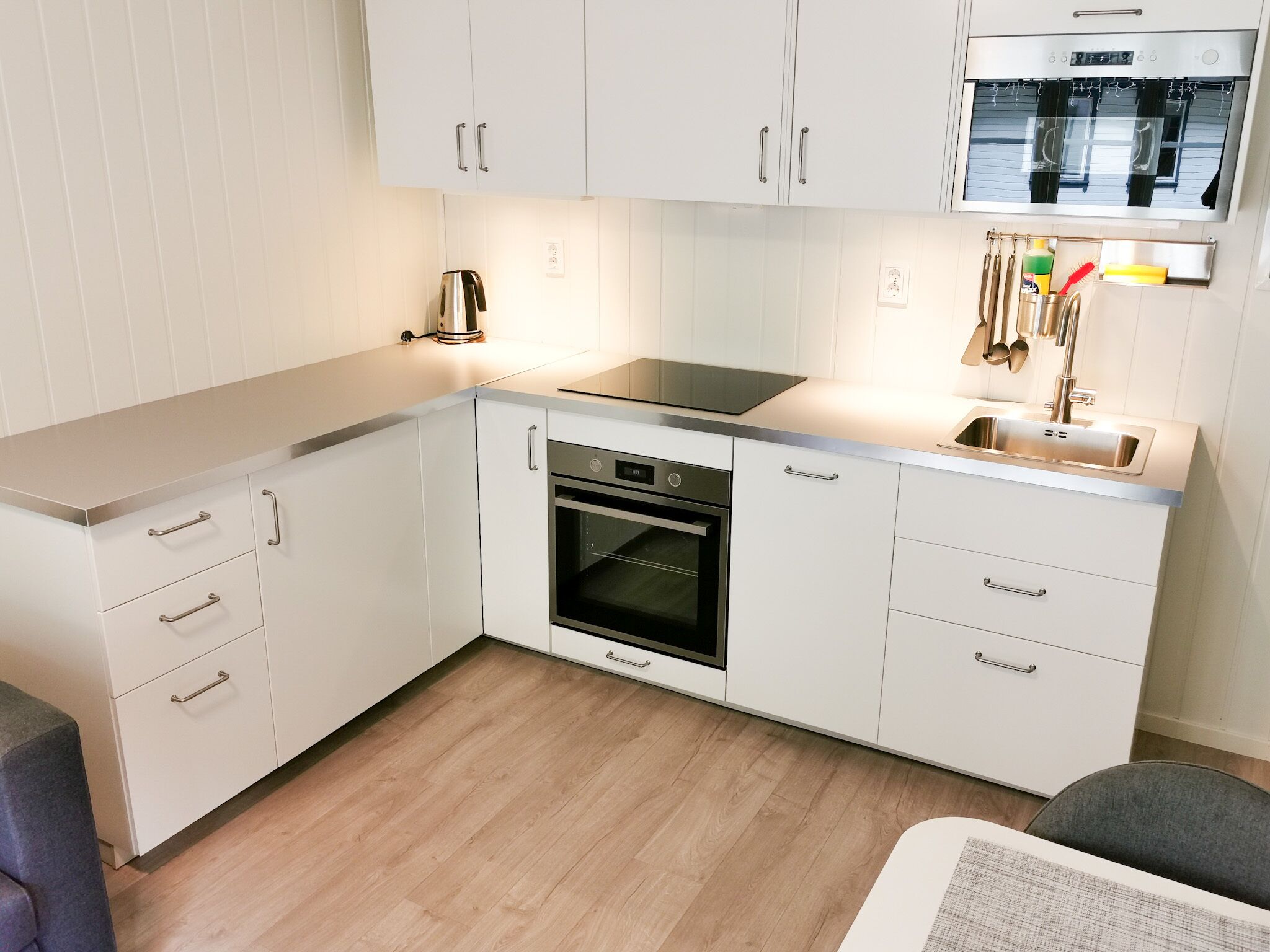 A compact kitchen with white cabinetry, a built-in oven, a microwave, and a sink.