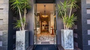 A modern entrance with a checkered floor leading to a hallway, flanked by tall potted plants and a glass door. - Mountview Guest House (Cape Town)