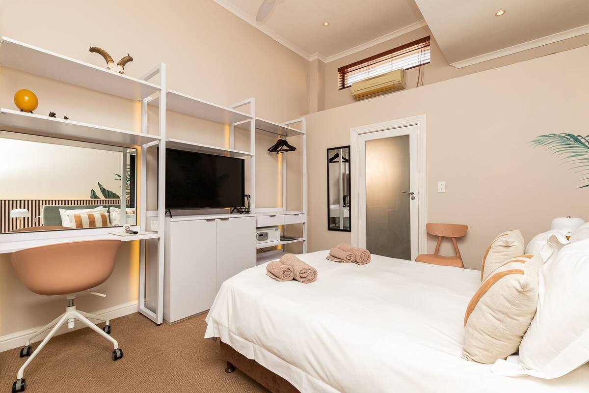Habitació d'hotel moderna amb un llit, escriptori amb televisió de pantalla plana, armari i bany amb mirall i barra de tovalloles.