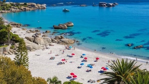 A beach with clear turquoise water, large rocks, and people relaxing under umbrellas. - Mountview Guest House (Cape Town)