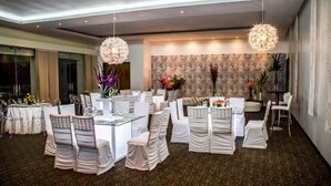 Un'ampia sala da pranzo con tavoli e sedie rotonde, eleganti lampadari e una parete decorata sullo sfondo.