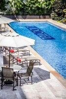 Piscina com área de descanso com mesas e cadeiras, rodeada por vegetação exuberante.