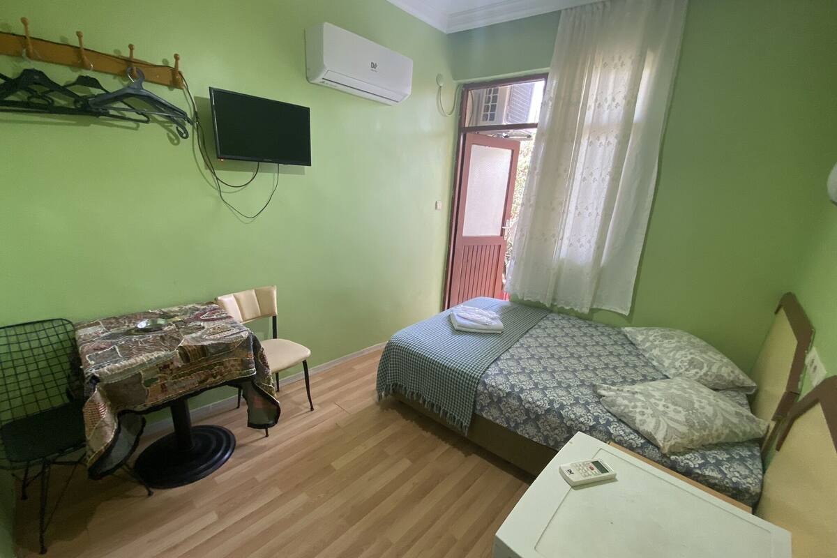 Ein kleiner Raum mit grünen Wänden, ausgestattet mit einem Bett, einem Tisch mit Stühlen, einem Fernseher und einem Fenster mit Vorhängen.