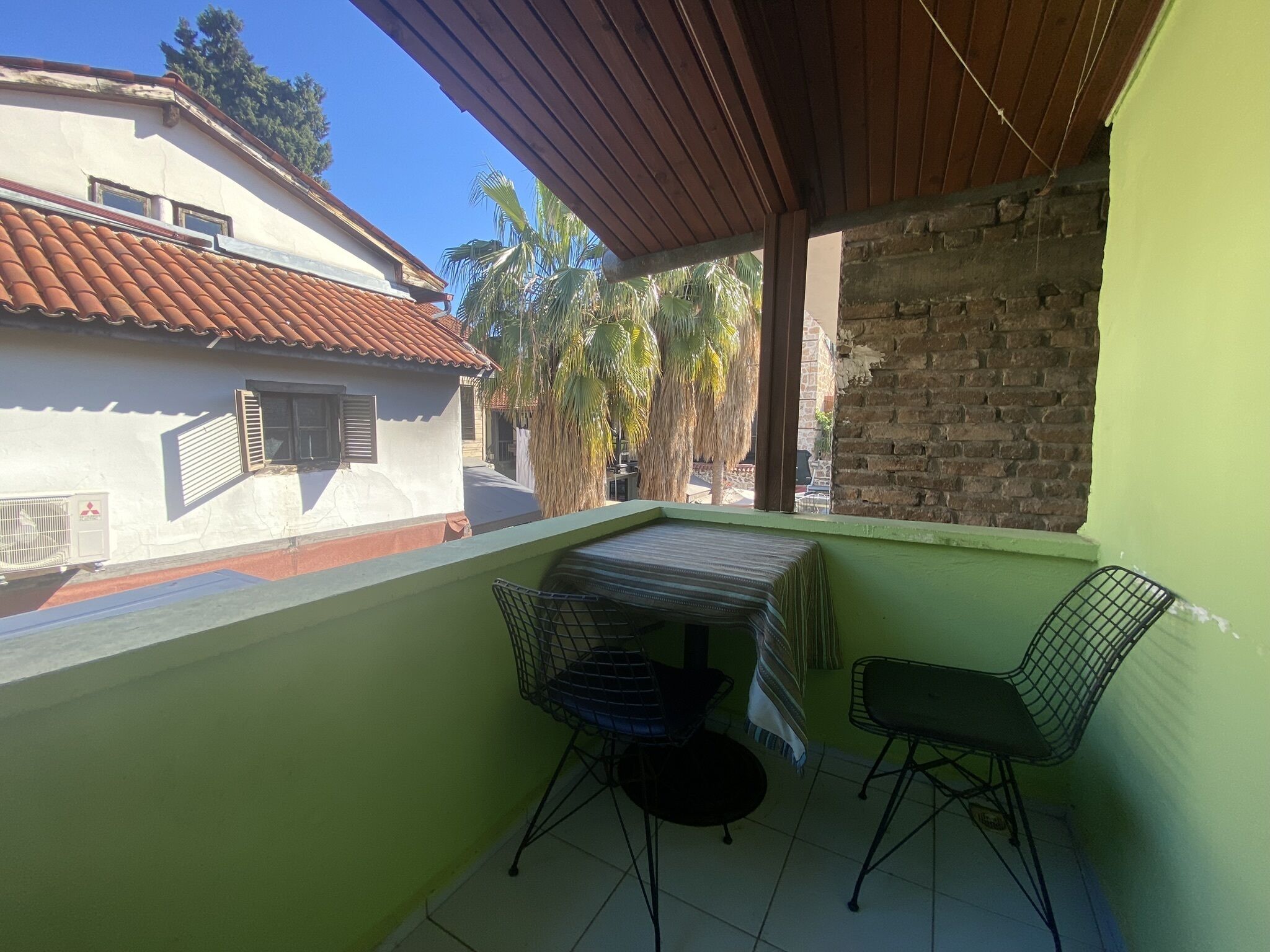 A balcony with a table and two chairs, a view of a neighboring building, and a palm tree.