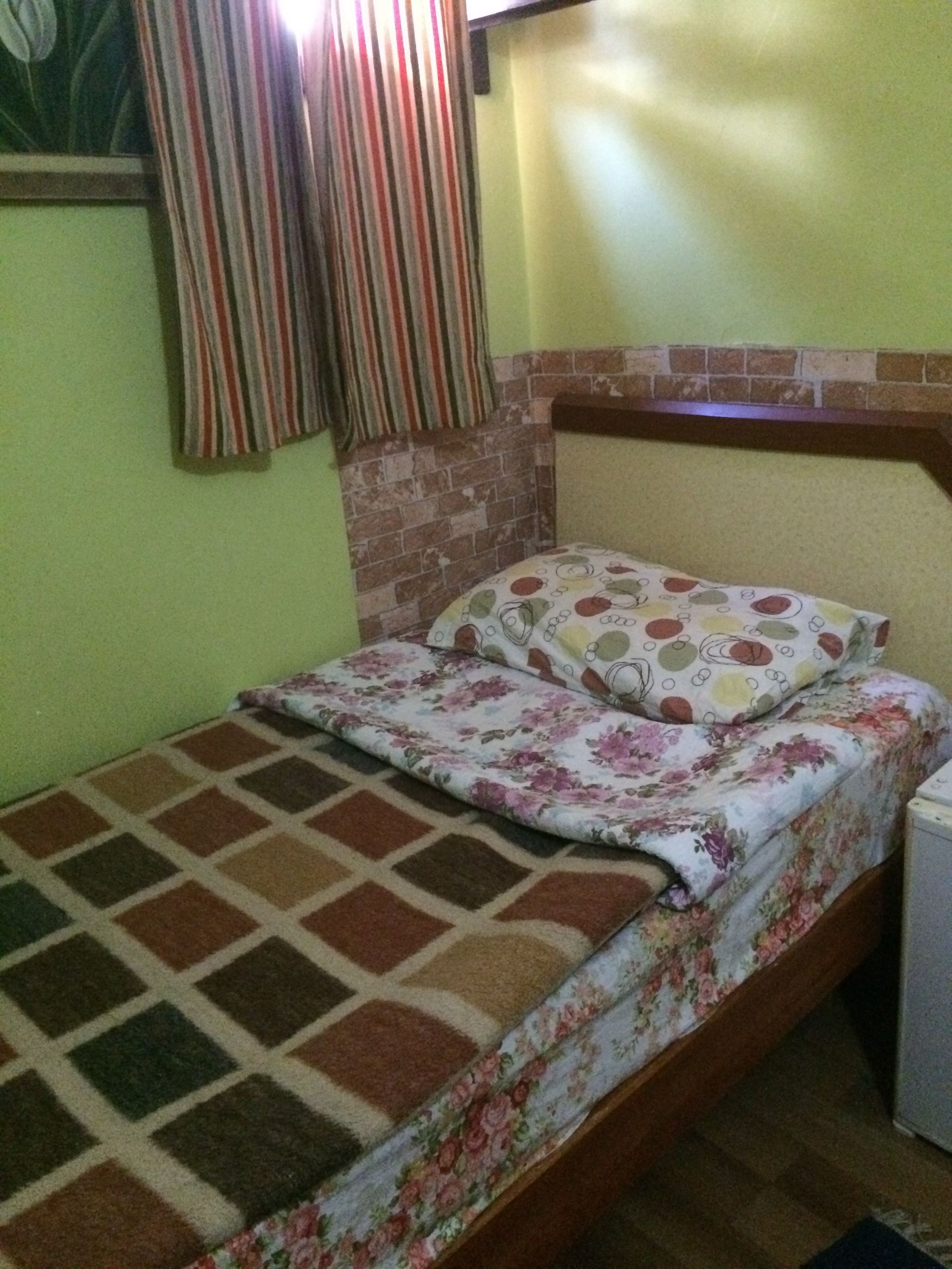 A bed with floral bedding, a striped curtain, and a brick-patterned headboard.